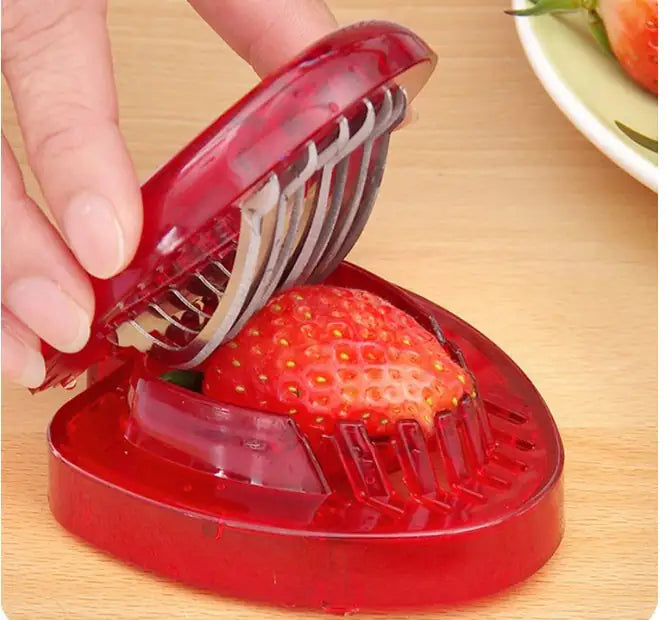 Red strawberry huller being used to remove a strawberry from its stem on a wooden surface.