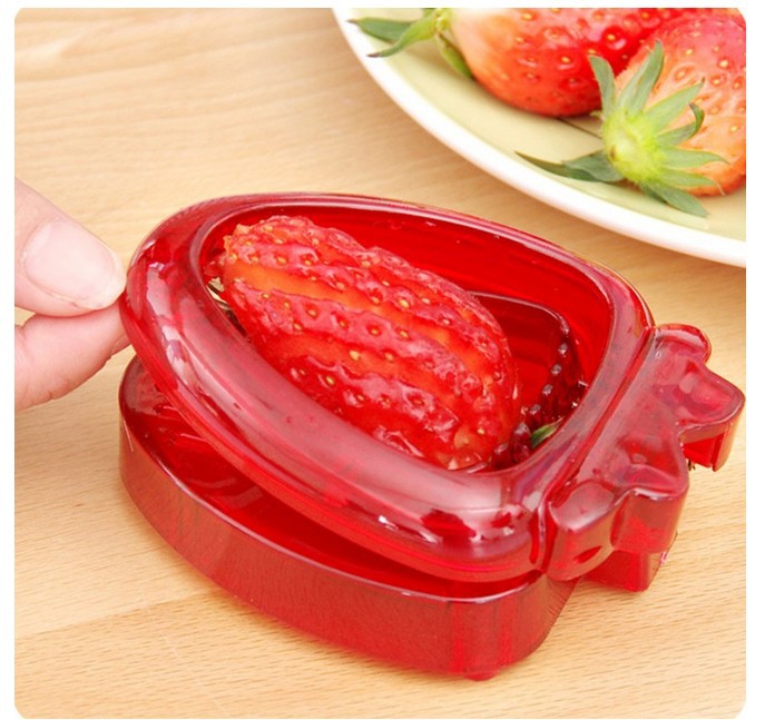 Red strawberry huller being used on a strawberry with more strawberries in the background.
