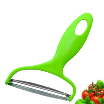 A bright green vegetable peeler with a stainless steel blade, shown on a white background with a small cluster of red tomatoes and green basil leaves in the bottom right corner.