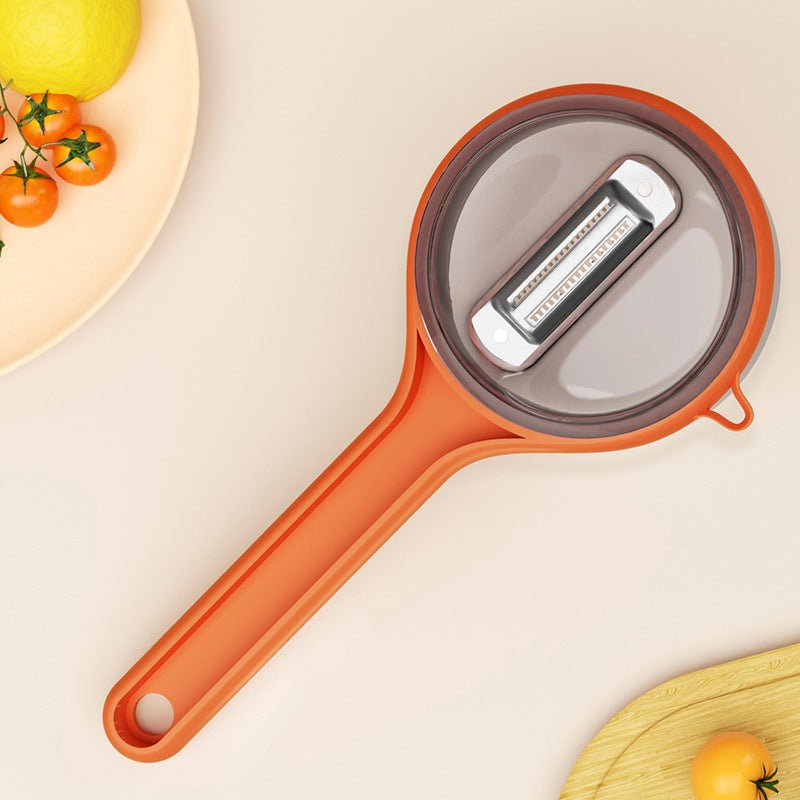 Orange vegetable peeler on a light beige background with tomatoes and lemons.