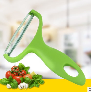 A green handheld vegetable peeler with a clear glass blade, shown over a yellow banner with fresh tomatoes, basil, and garlic against a blurred kitchen background.