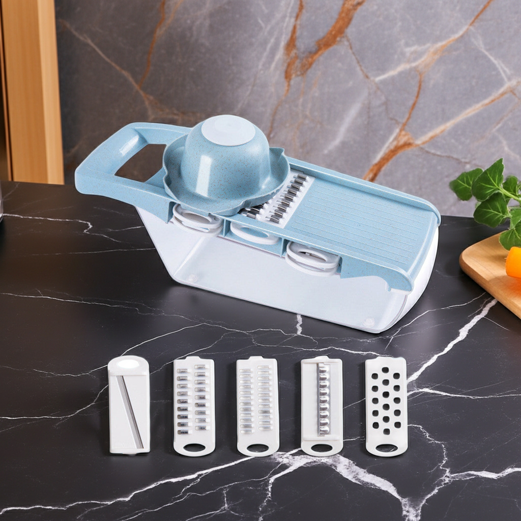 A plastic vegetable slicer/dicer set with a light blue and white main unit, shown on a dark marble countertop with four interchangeable blade attachments in front. A marble backsplash and small garnish props are visible in the background.