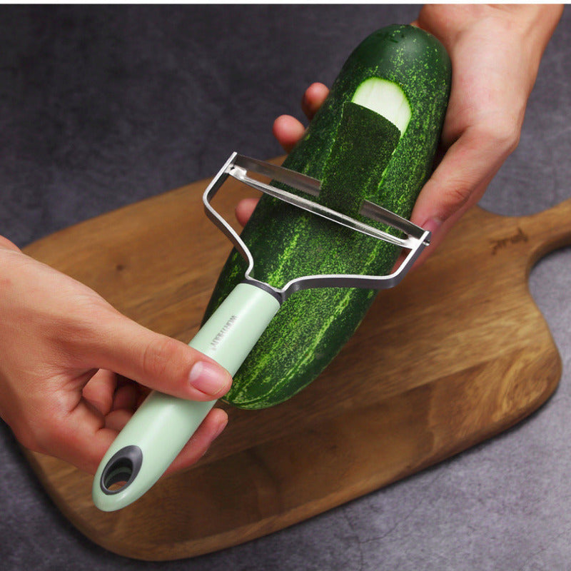 Person using a vegetable peeler on a zucchini on a wooden cutting board.