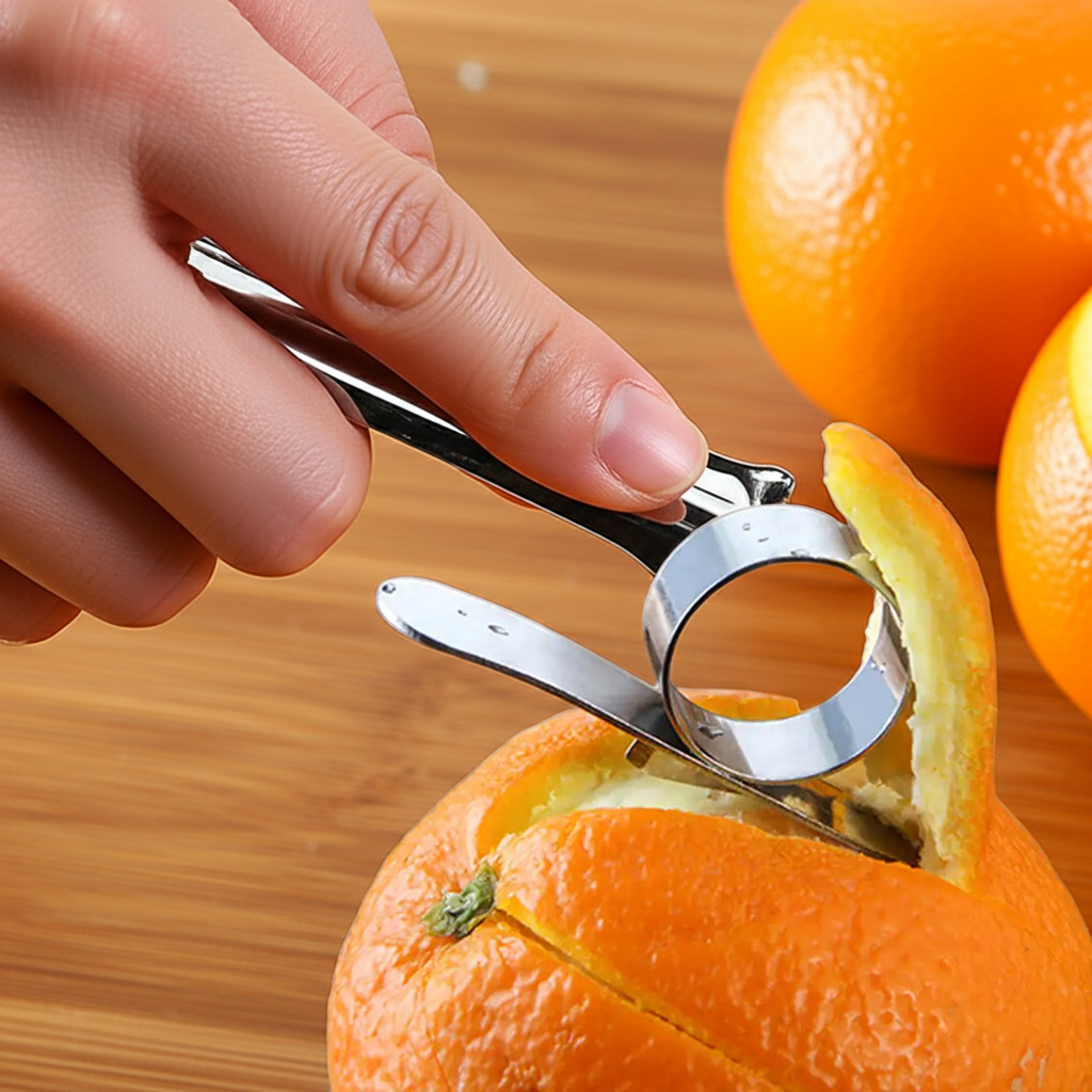 A close-up of a hand using a stainless steel citrus peeler tool to remove an orange peel from an orange, with whole oranges blurred in the background on a wooden surface.