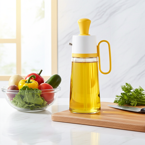 A clear glass oil dispenser filled with golden yellow oil, featuring a white body and bright yellow cap and handle, set on a wooden cutting board in a bright kitchen scene with fresh vegetables nearby.