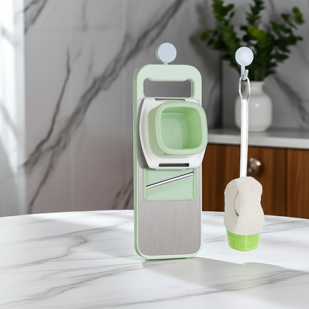 A kitchen slicing and chopping set on a white marble countertop, featuring a mint green and white mandoline-style slicer with a brushed stainless steel blade, and a matching cleaning brush with a white sponge head and green base.