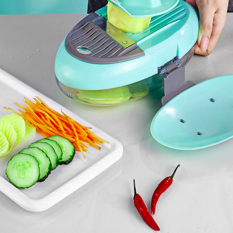 Vegetable slicer cutting vegetables on a kitchen counter with sliced cucumbers, carrots, and red peppers.
